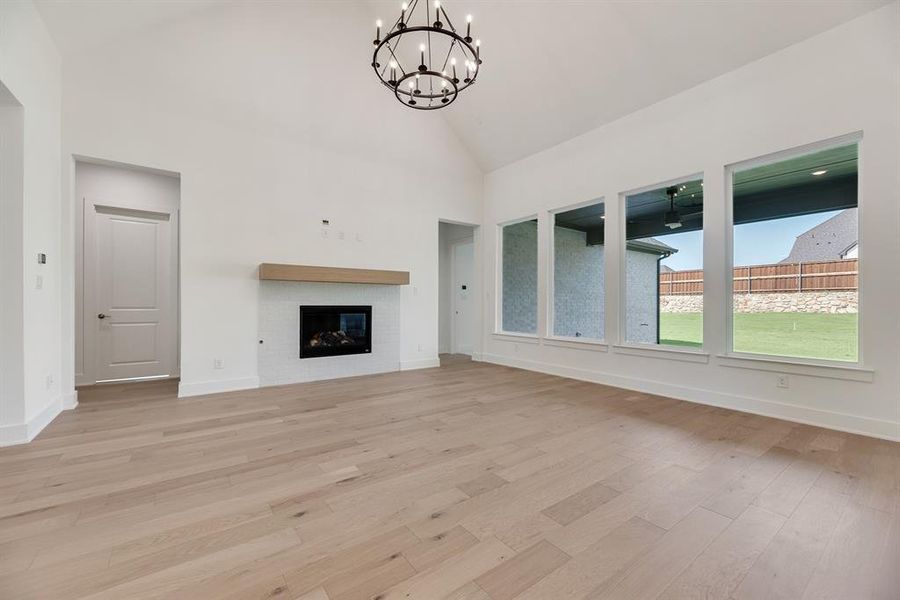 Unfurnished living room featuring high vaulted ceiling, a glass covered fireplace, light wood finished floors, and a chandelier