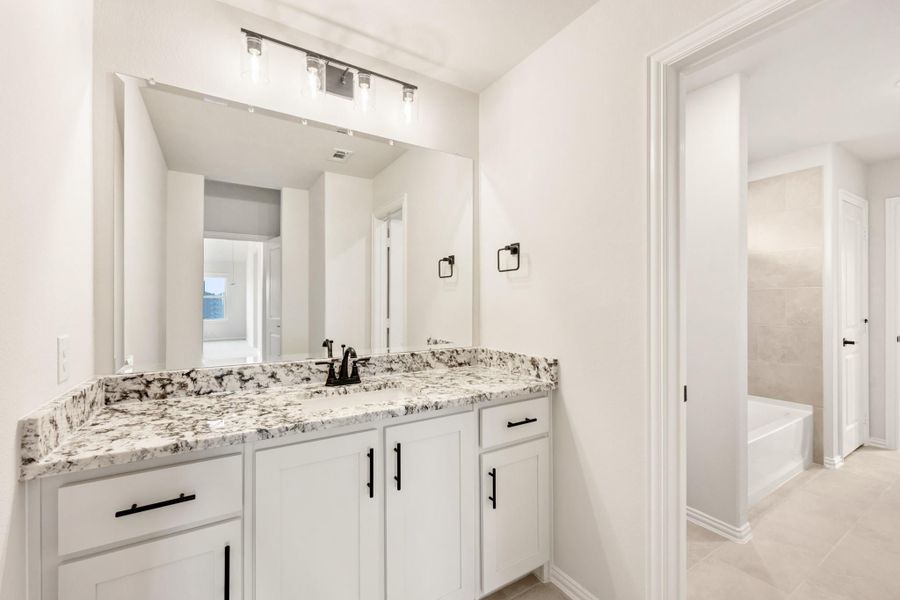 Bathroom with white cabinets, granite countertop, large mirror, and soaking tub in adjacent alcove Bathroom with white cabinets, granite countertop, large mirror, and soaking tub in adjacent alcove
