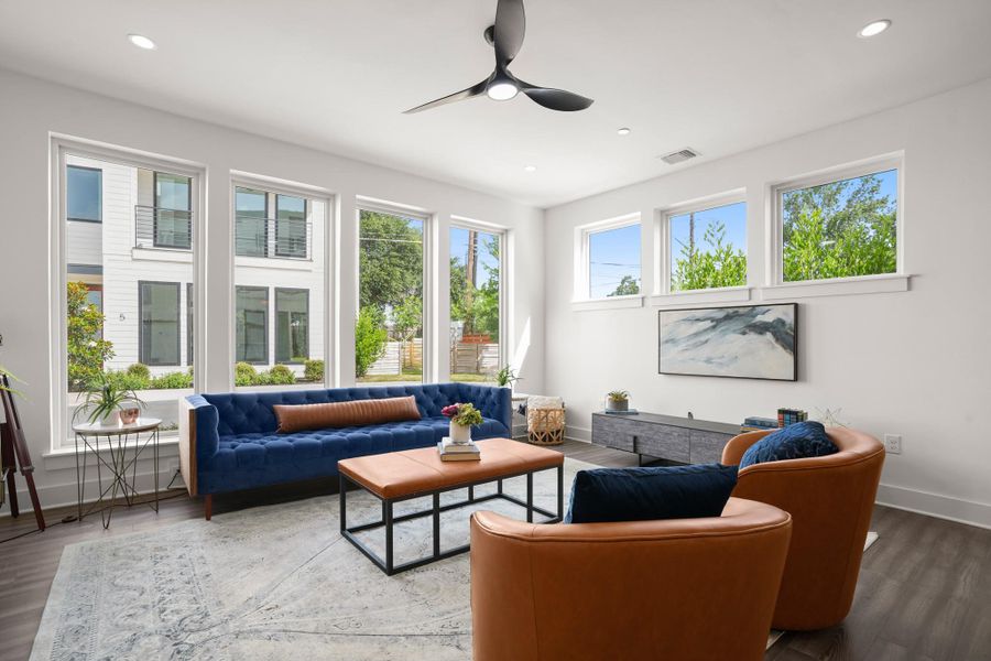 A well-lit living space, featuring high ceilings and dark hardwood flooring, offers views of the exterior through multiple large windows. A well-lit living space, featuring high ceilings and dark hardwood flooring, offers views of the exterior through multiple large windows.