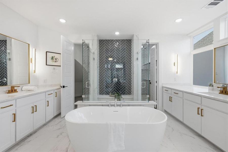 Spacious bathroom featuring a freestanding soaking tub, dual vanities with white cabinetry and light-colored countertops, a glass-enclosed shower with a herringbone tile accent wall, and large format tile flooring