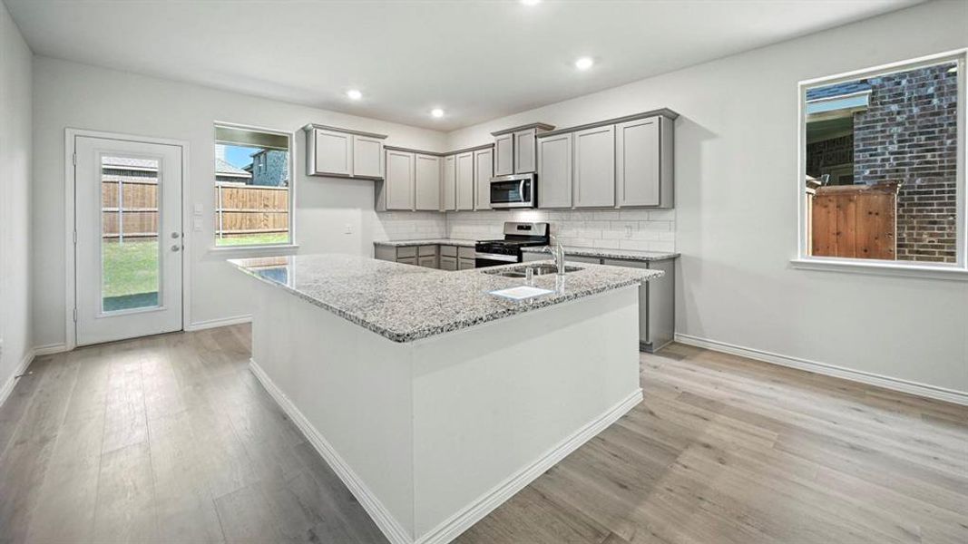 Kitchen with gray cabinetry, light stone countertops, stainless steel appliances, backsplash, and light wood-style floors Kitchen with gray cabinetry, light stone countertops, stainless steel appliances, backsplash, and light wood-style floors