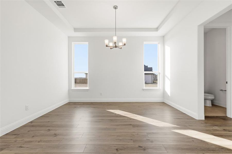 Unfurnished dining area with suspended lighting, a raised ceiling, healthy amount of natural light, and dark wood finished floors Unfurnished dining area with suspended lighting, a raised ceiling, healthy amount of natural light, and dark wood finished floors