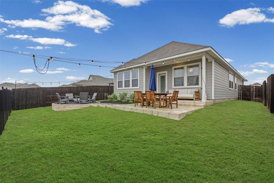 Expansive backyard featuring a manicured lawn, full privacy fencing, a covered concrete patio, a raised concrete patio, and a stone fire pit area