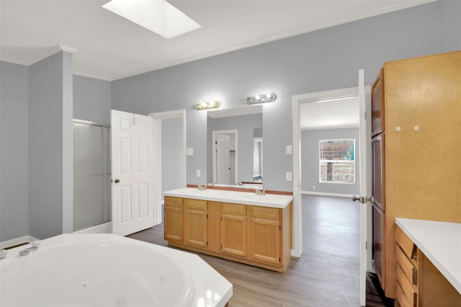 Full bathroom with a skylight, double vanity, a tub with jets, dark wood-style flooring, and a stall shower