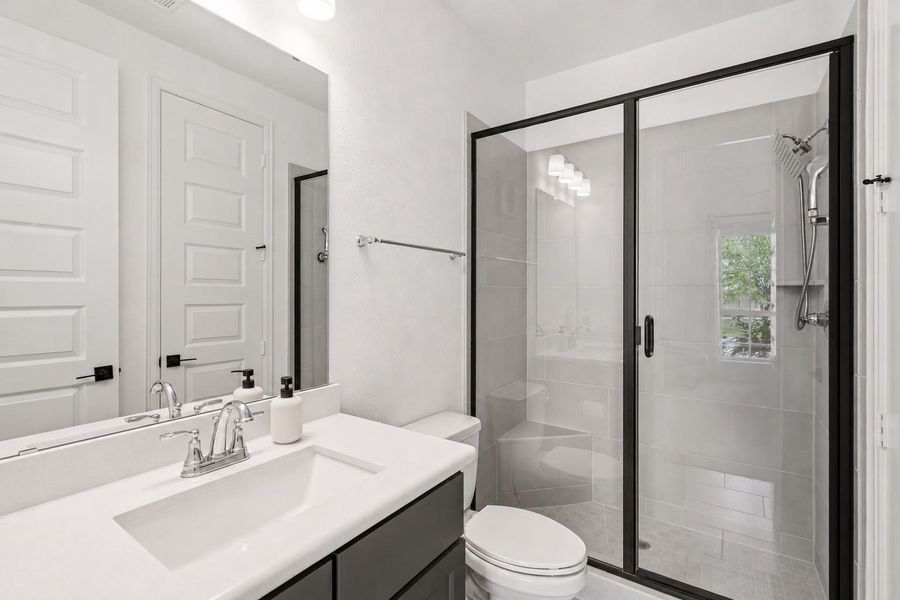 Relax and unwind in this downstairs secondary bedroom’s ensuite bathroom, featuring elegant quartz countertops and a spacious glass surround walk in shower for the ultimate in comfort and style, complete with a full walk in closet.