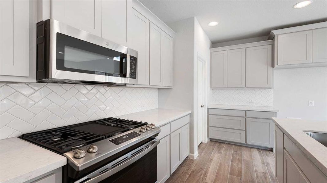 Kitchen with light wood-type flooring, backsplash, stainless steel appliances, and light stone countertops