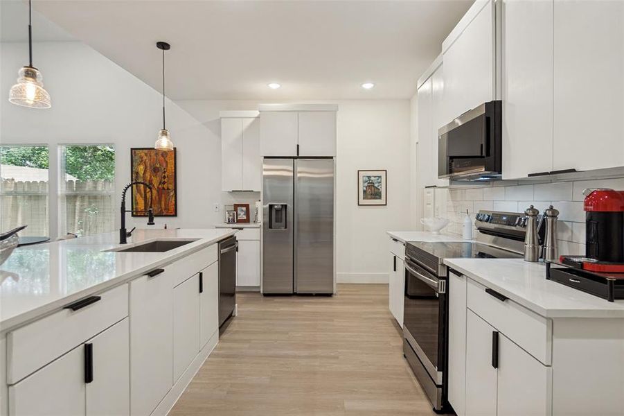 Kitchen featuring white cabinetry, quartz countertops, stainless steel appliances, wood-finish flooring, and a vaulted ceiling Kitchen featuring white cabinetry, quartz countertops, stainless steel appliances, wood-finish flooring, and a vaulted ceiling