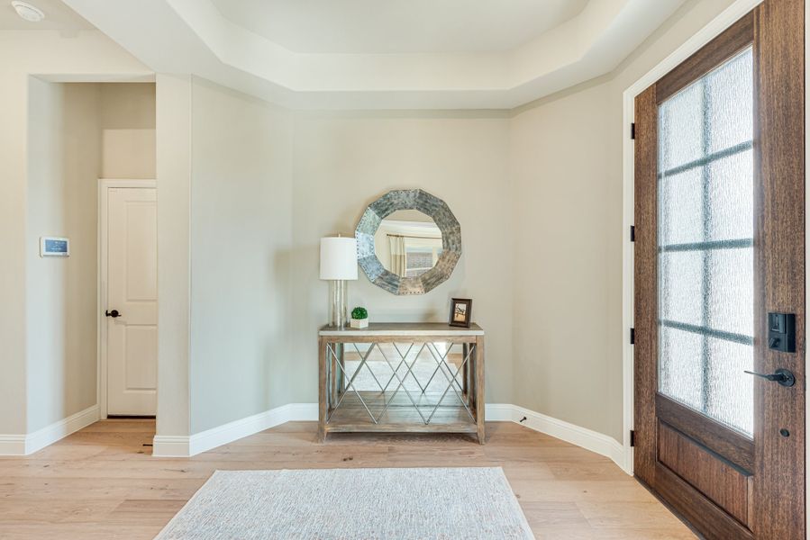 Home entryway with wood front door, console table, round mirror, and tray ceiling over light hardwood floors
