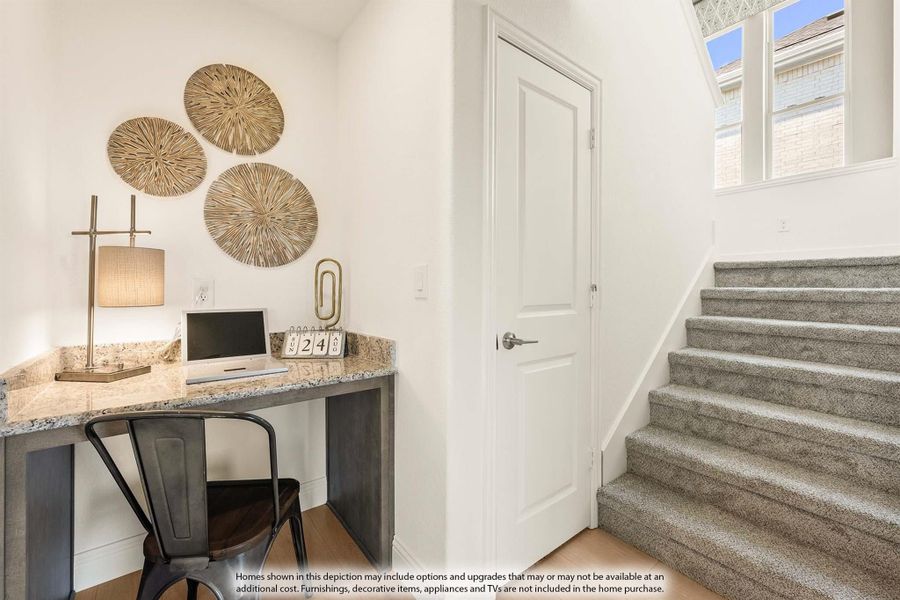 Built-in granite desk nook with metal chair beside carpeted staircase and white walls with decorative wall art