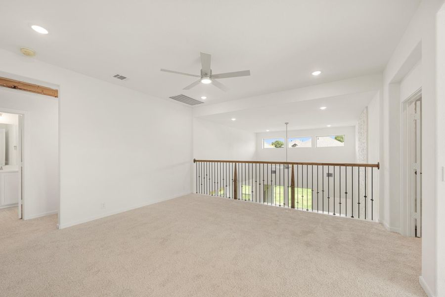 Open upstairs loft with carpet flooring, ceiling fan, and iron baluster railing overlooking lower level