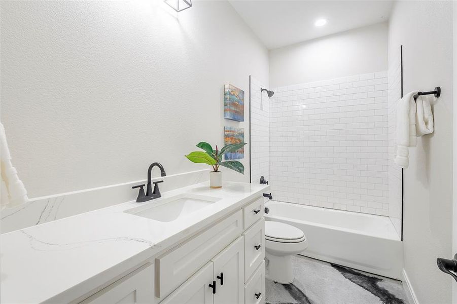 Full bathroom with granite vanity, tiled shower / bath combo, and toilet