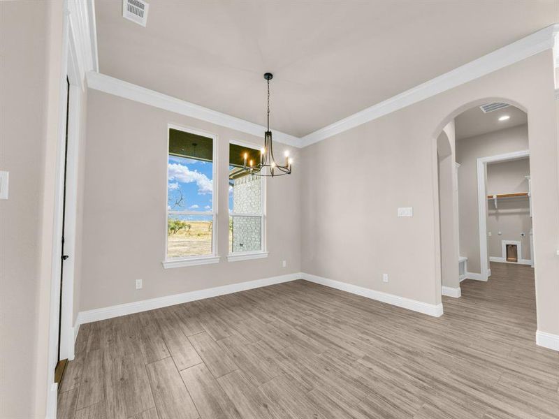 Empty room with light hardwood / wood-style floors, an inviting chandelier, and ornamental molding