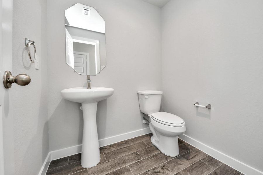 This half bathroom features a stylish pedestal sink, modern hardware, and bright recessed lighting, creating a sleek and inviting space.