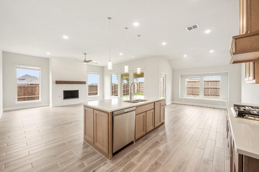 Open-concept kitchen with center island, wood cabinets, and light floors flowing into living area with fireplace