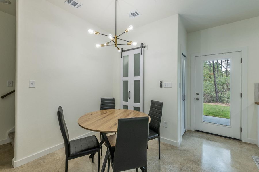Open-concept dining area featuring a modern sputnik chandelier, a white barn door with frosted glass panels, and a full-light exterior door Open-concept dining area featuring a modern sputnik chandelier, a white barn door with frosted glass panels, and a full-light exterior door