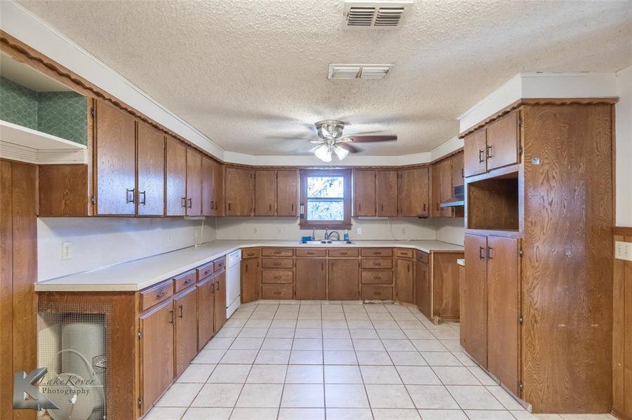 Kitchen with brown cabinetry, a textured ceiling, light tile patterned flooring, light countertops, and ceiling fan Kitchen with brown cabinetry, a textured ceiling, light tile patterned flooring, light countertops, and ceiling fan