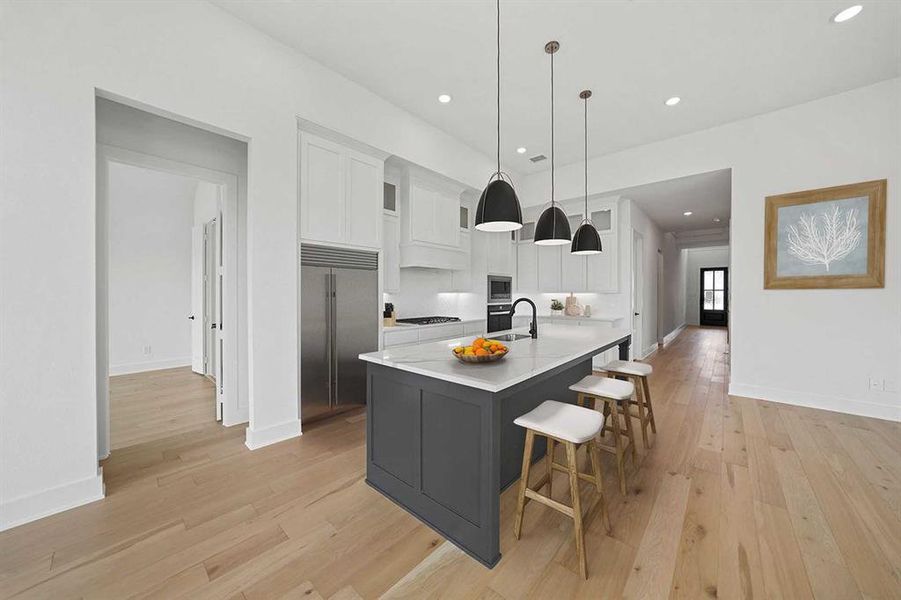 Kitchen featuring white cabinets, a breakfast bar area, built in appliances, a center island with sink, and recessed lighting Kitchen featuring white cabinets, a breakfast bar area, built in appliances, a center island with sink, and recessed lighting