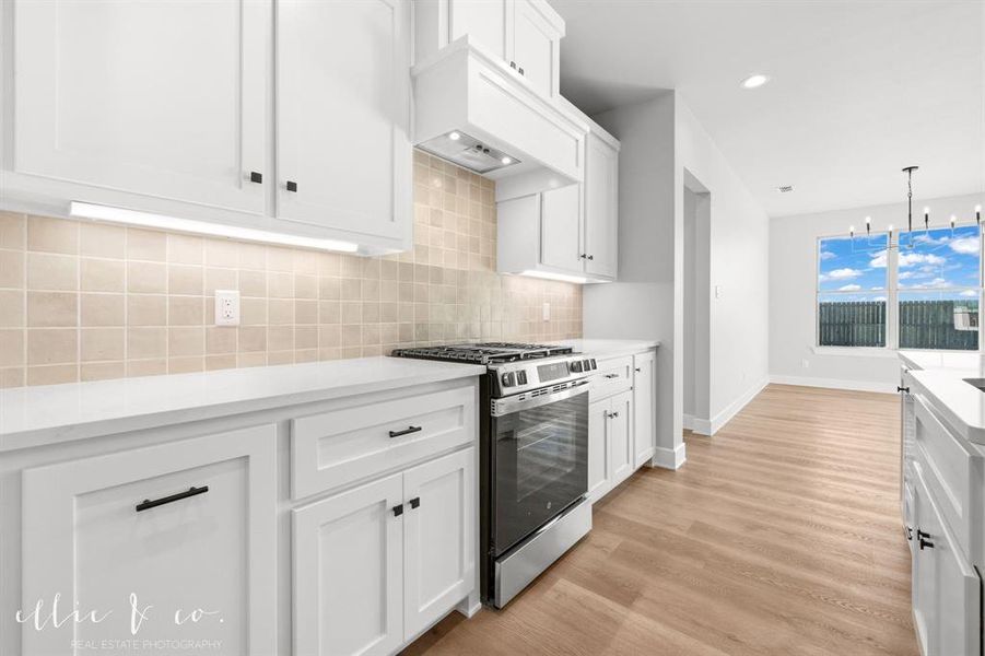 Kitchen with white cabinetry, stainless steel gas range, backsplash, light wood-type flooring, and hanging light fixtures