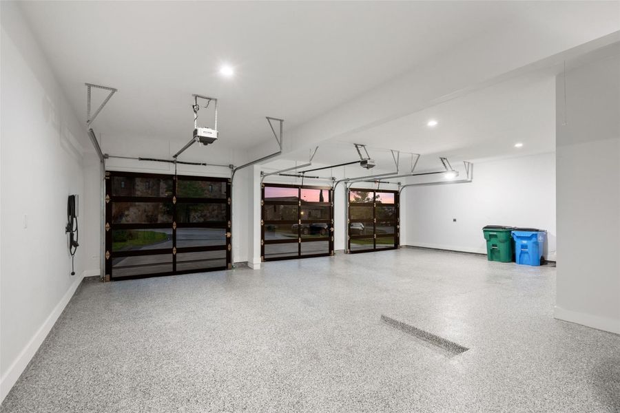 Spacious garage featuring a durable epoxy floor finish, three glass panel garage doors, recessed ceiling lighting, and an electric vehicle charging station