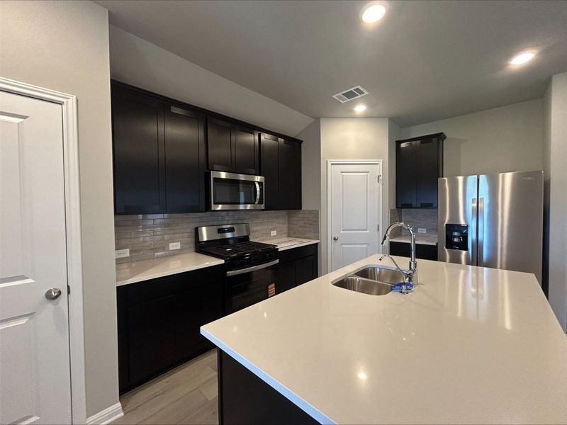 Kitchen featuring dark cabinetry, stainless steel appliances, light countertops, backsplash, and recessed lighting Kitchen featuring dark cabinetry, stainless steel appliances, light countertops, backsplash, and recessed lighting