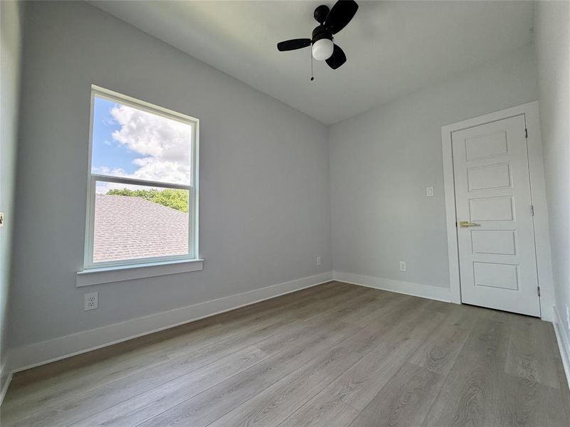 Spacious room featuring wood-finish flooring, a contemporary ceiling fan, and a single window providing natural light Spacious room featuring wood-finish flooring, a contemporary ceiling fan, and a single window providing natural light