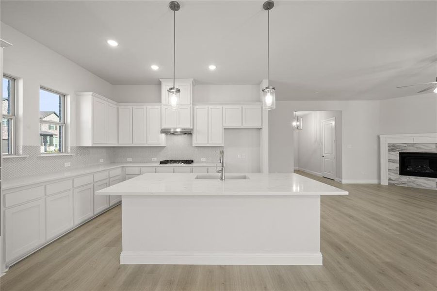 Kitchen with sink, a fireplace, an island with sink, decorative light fixtures, and white cabinetry