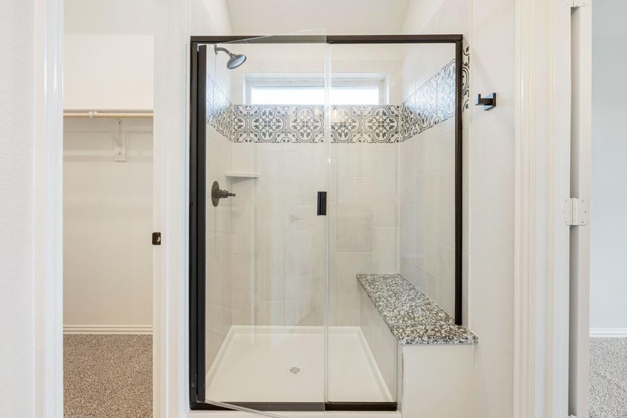 Walk-in shower with black frame glass door, white tile, decorative accent tile border, and built-in granite bench seat