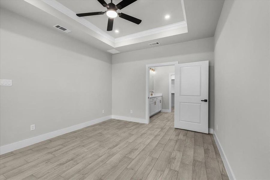 Unfurnished bedroom featuring baseboards, visible vents, a tray ceiling, crown molding, and light wood-type flooring