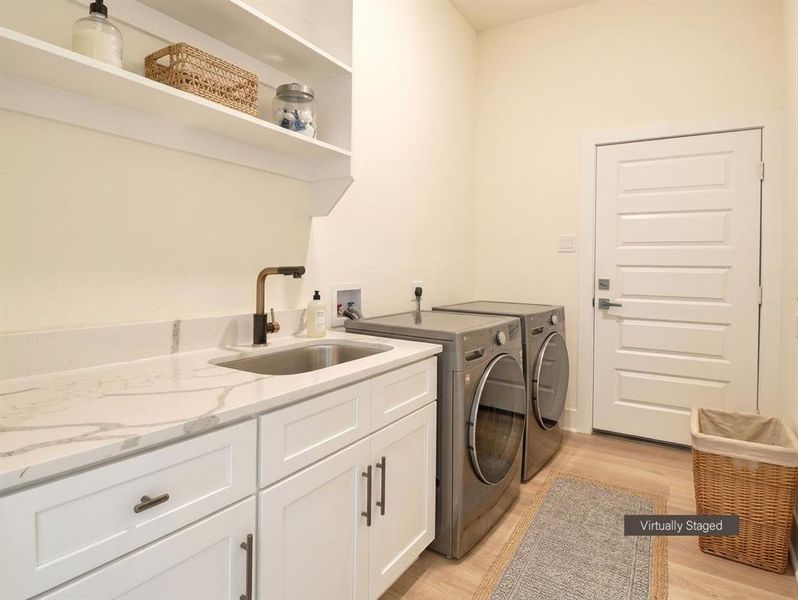 Laundry room featuring a deep utility sink, white shaker-style cabinetry, and a stone-finish countertop with veining