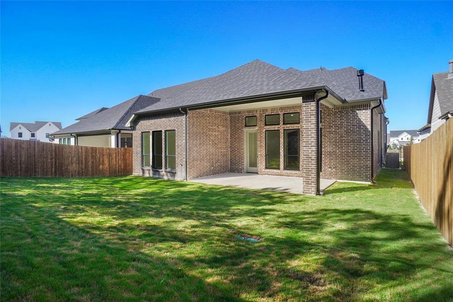 Back of property with a fenced backyard, brick siding, a patio area, and roof with shingles