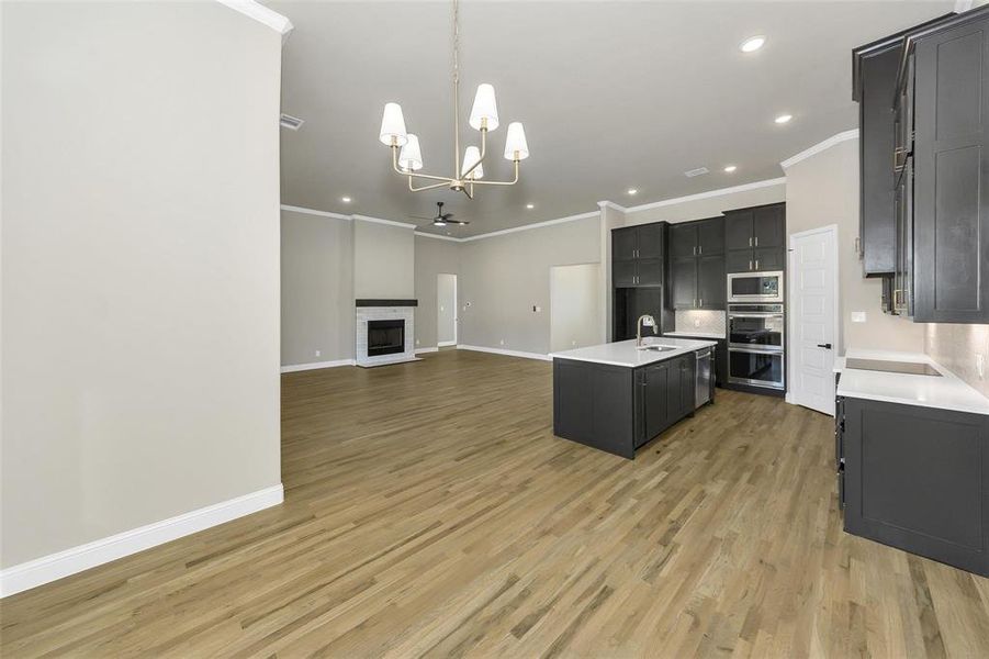 Kitchen featuring dark cabinetry, open floor plan, crown molding, decorative light fixtures, and a kitchen island with sink