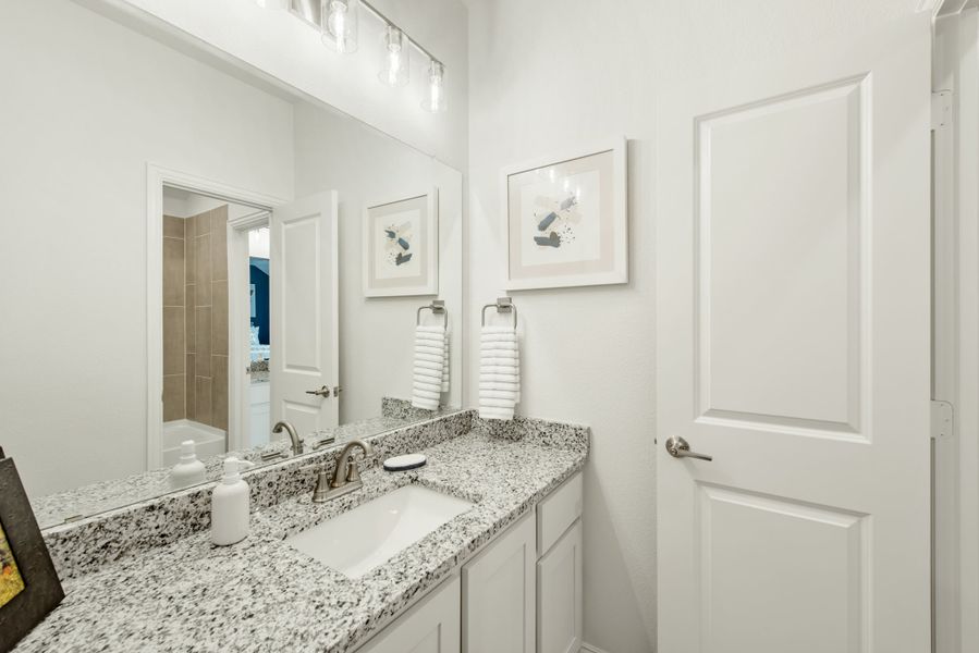 Bathroom vanity with granite countertop, white cabinets, single sink, and large mirror with overhead lighting