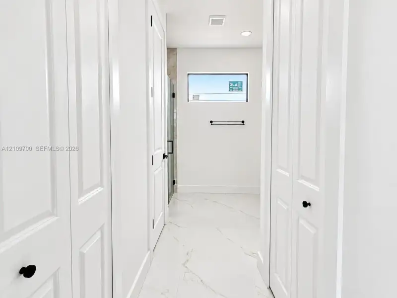 Hallway featuring white paneled doors with matte black hardware, large-format tile flooring with marble-style veining, recessed lighting, and a horizontal window