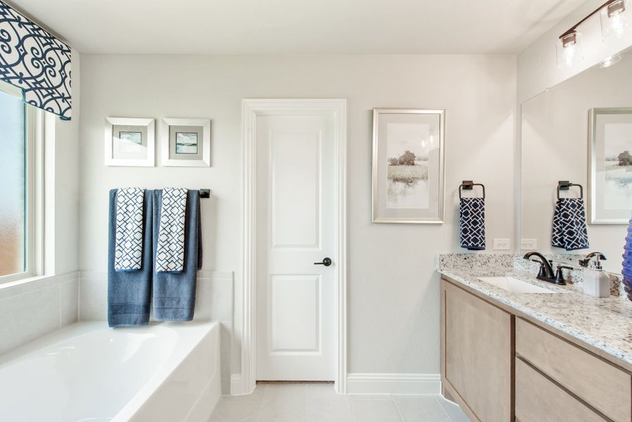 Bathroom with soaking tub, granite vanity, wood cabinets, and large mirror with blue accent towels