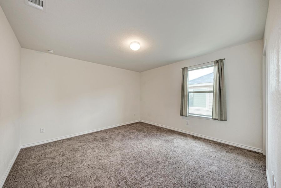 A well-lit bedroom with ample space, featuring soft carpet and a clear view from the window.