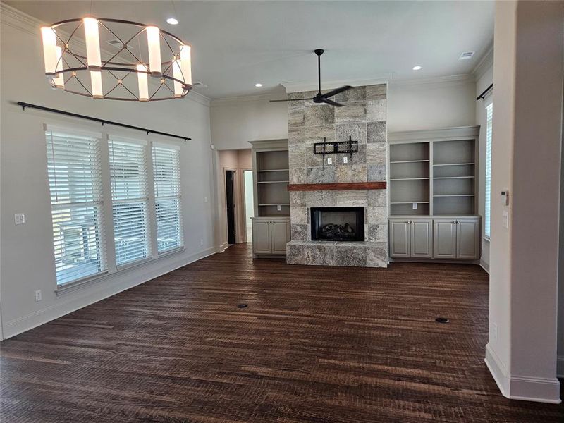 Unfurnished living room with a fireplace, dark hardwood / wood-style flooring, crown molding, an inviting chandelier, and built in features