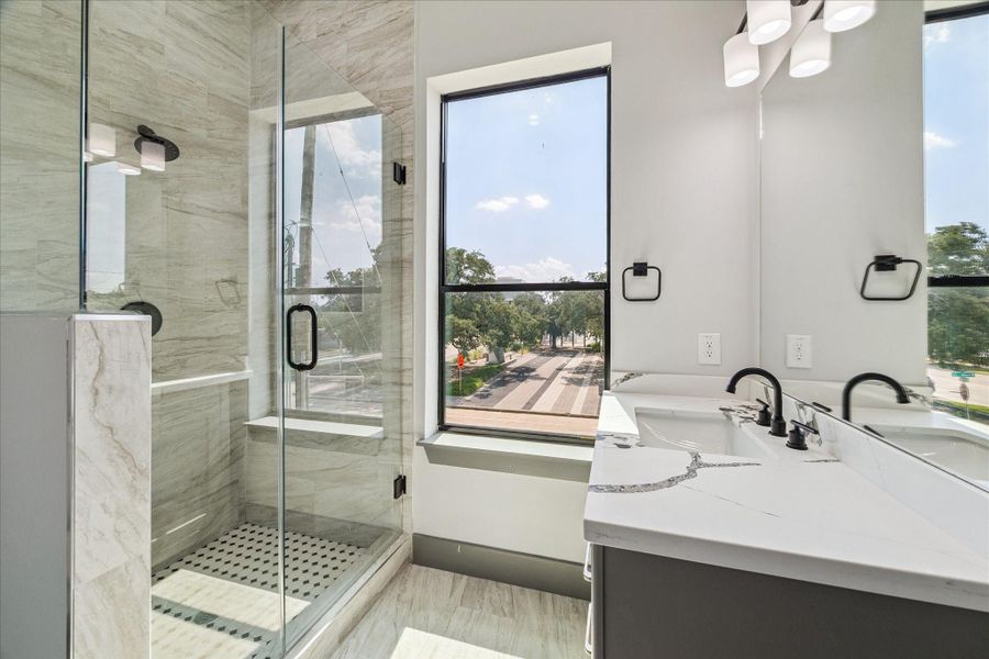 Glass-enclosed shower with contemporary tile and a quartz-style vanity highlight the modern design of this bathroom, while a large window adds openness and an outdoor view. Glass-enclosed shower with contemporary tile and a quartz-style vanity highlight the modern design of this bathroom, while a large window adds openness and an outdoor view.