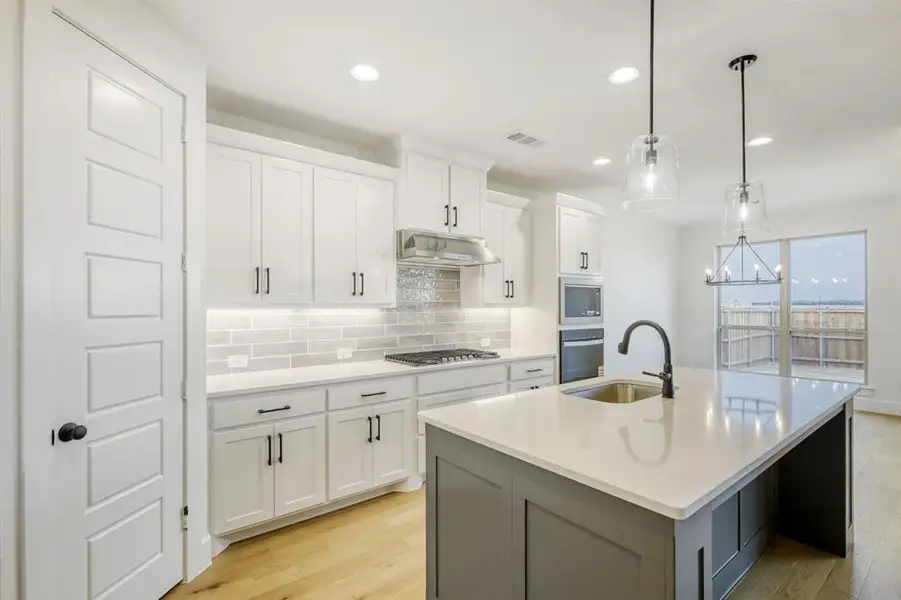 Two tone kitchen featuring light wood-type flooring, tasteful backsplash, a kitchen island with sink, stainless steel appliances, and two tone cabinets
