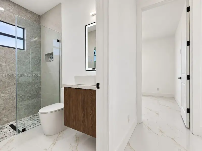 Bathroom featuring a floating vanity with a vessel sink, stone-finish shower surround, frameless glass shower enclosure, and oversized tile flooring