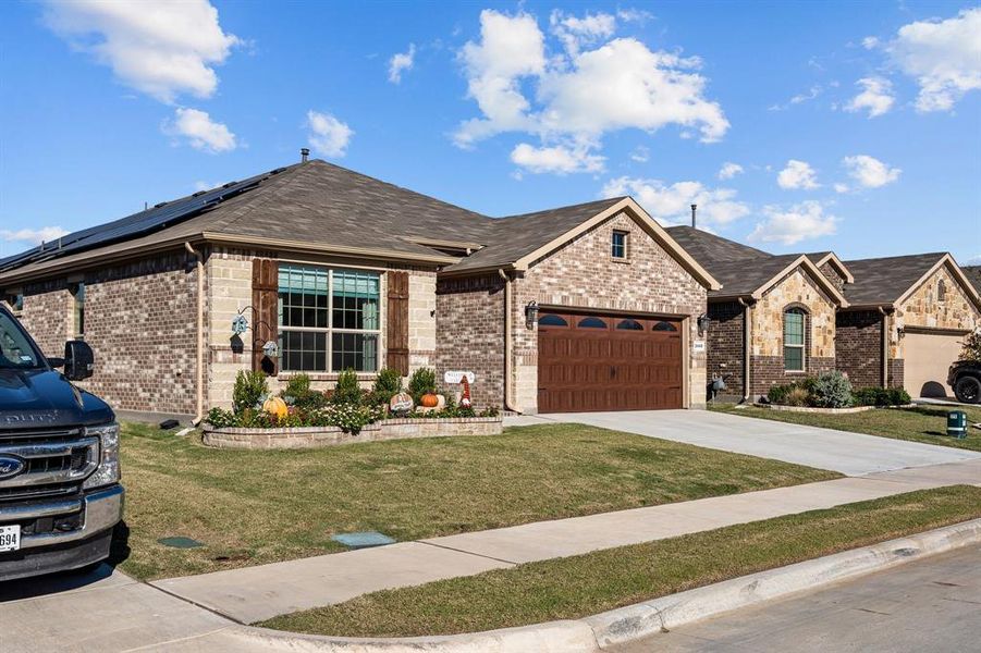 View of front of property with a front yard, solar panels, and a garage