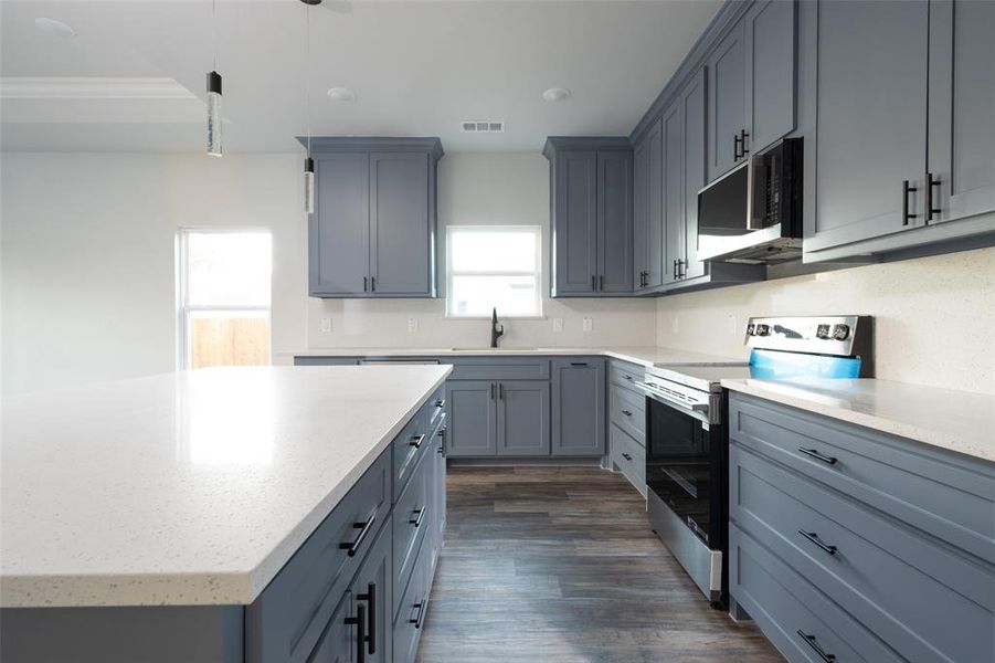 Kitchen featuring appliances with stainless steel finishes, light stone counters, dark wood finished floors, and decorative light fixtures