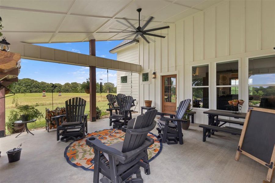 Expansive covered back porch designed for luxury outdoor living, featuring a wood-burning fireplace, generous seating space, ceiling fan, and peaceful acreage views—ideal for relaxing or entertaining year-round.