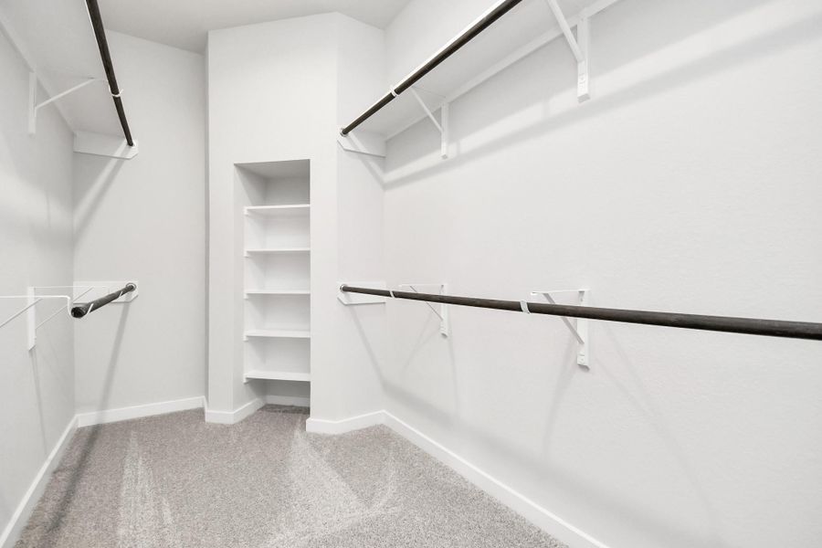 Experience luxury in this spacious walk-in closet with high ceilings and plush carpet. Warm paint tones, built-in shelving, and dark finishes create a contemporary and functional retreat. Sample photo of completed home with similar floor plan. Actual colors and selections may vary.