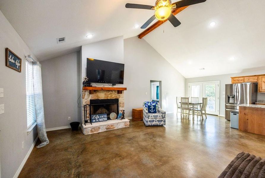 Living area featuring a fireplace, concrete floors, beamed ceiling, high vaulted ceiling, and a ceiling fan