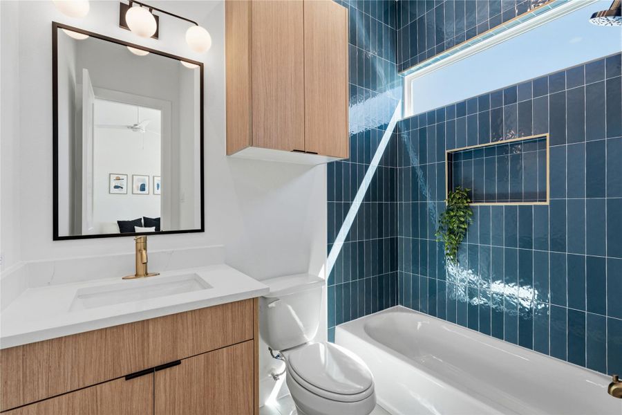 The architecture utilizes floor-to-ceiling blue vertical tiling in the tub-shower alcove to create a bold focal point. A light oak vanity and white stone countertop are accented by brushed gold hardware and modern globe lighting.