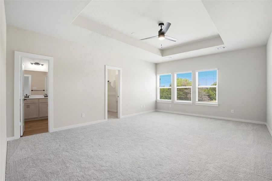 Unfurnished bedroom featuring a raised ceiling, light colored carpet, connected bathroom, and ceiling fan Unfurnished bedroom featuring a raised ceiling, light colored carpet, connected bathroom, and ceiling fan