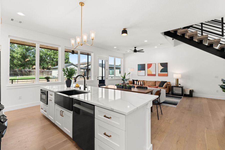 This open-concept living area features a modern kitchen with a large island and sleek finishes, seamlessly connected to a bright living room with ample natural light. Perfect for entertaining, the space overlooks a lush backyard through large windows, and includes a stylish staircase leading to the upper level.