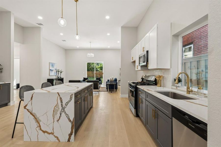 Contemporary kitchen featuring a waterfall island with a patterned stone countertop, two-tone cabinetry, stainless steel appliances, and wood-finish flooring Contemporary kitchen featuring a waterfall island with a patterned stone countertop, two-tone cabinetry, stainless steel appliances, and wood-finish flooring