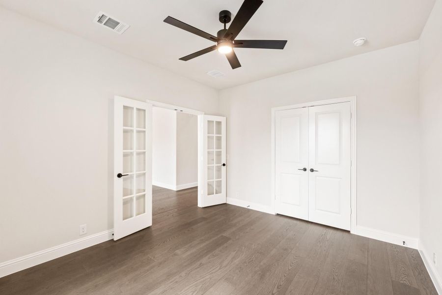 Empty bedroom with dark hardwood floors, ceiling fan, French doors, and a double-door closet