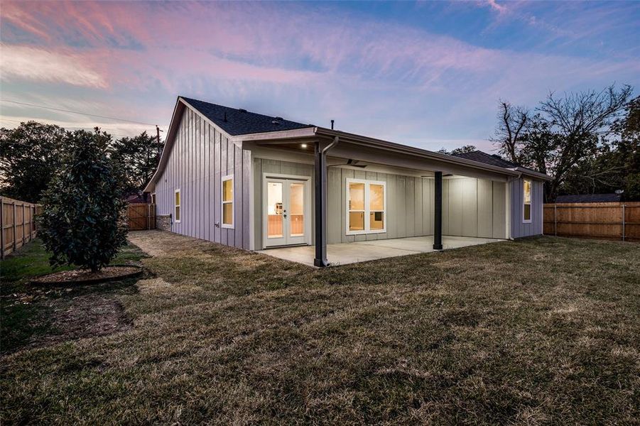 Back house at dusk with a patio area and a lawn